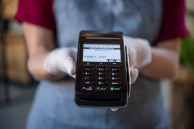 Kafeterya çalışanlarının ellerini kapatın. Bağlantı kurulamayan kredi kartı ve NFC teknolojisiyle ödeme için pozisyon gösteriyorlar. Garson, tek kullanımlık koruyucu eldivenler giyiyor ve restoranda kredi kartı okuyucu makinesi tutuyor. Yayılmanın sosyal mesafesi ve önlenmesi