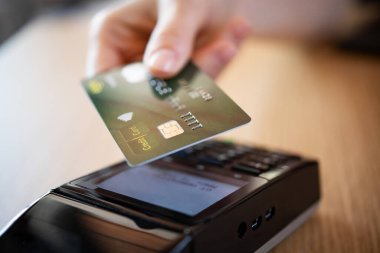 Faturayı kredi kartıyla ödeyen kadının elini kapat. Müşterinin eli, terminal cihazında NFC teknolojisiyle irtibatsız kredi kartıyla ödeme yapıyor. Kahve dükkanında ya da restoranda kart okuyuculu cep telefonu ödemesinin kapatılması.