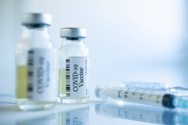 Laboratuvardaki COVID-19 koronavirüs aşı tüplerini kapatın. Sars-CoV-2 aşılı şırınga ve şişe klinik deneye hazır. Şişede bir doz aşı, cam sehpanın üzerinde de fotokopi alanı var..