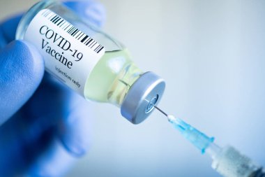 Doktor cam şişeden Covid-19 aşısı hazırlıyor ve aşı için şırınga dolduruyor. Laboratuvarda tek kullanımlık koruyucu eldivenler giyerek ve elinde bir şişe aşı ilacı tutarak. Mavi cerrahi eldivenli bir el...