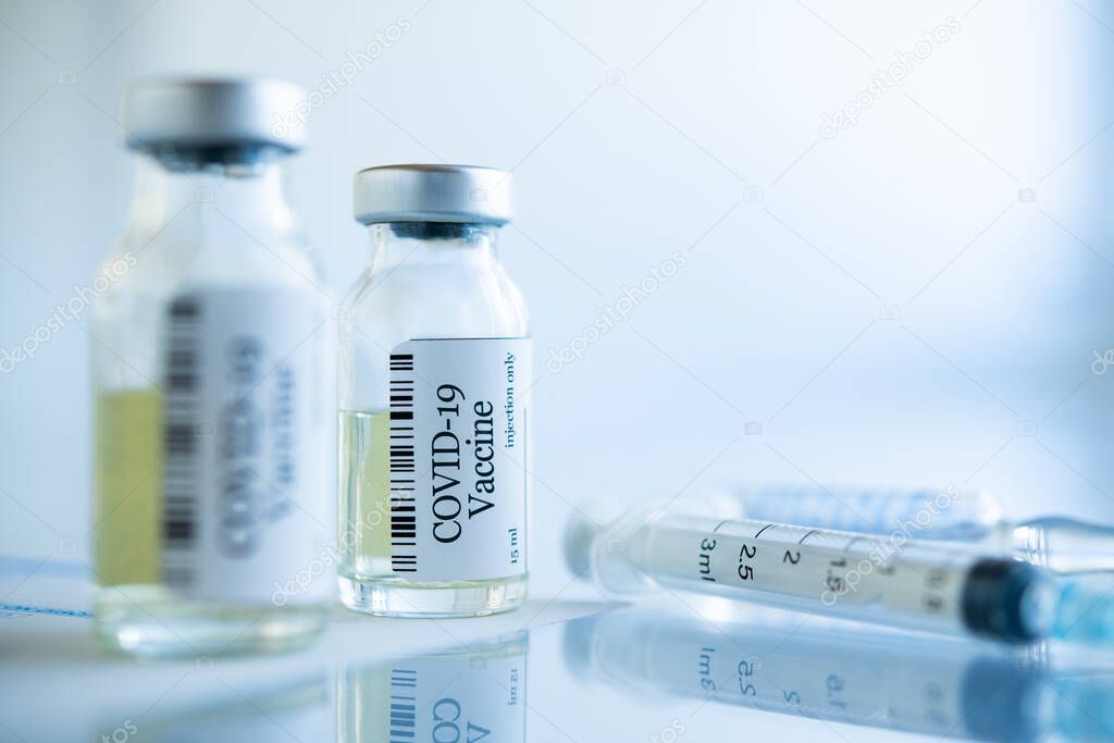 Close up of COVID-19 coronavirus vaccine vials at the lab. Syringe and phial with virus Sars-CoV-2 vaccine ready for clinical trial. One dose of vaccine in vial with syringe on glass table with copy space.