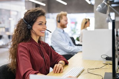 Servis masası danışmanı telefonla konuşuyor. Gülümseyen çağrı merkezi operatörü yardım hattında çalışıyor. Modern bir ofiste üst üste oturan çağrı merkezi ajanları müşteri hizmetleri sunuyorlar..
