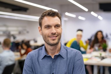 Ofiste dikilirken başka tarafa bakan düşünceli işadamının portresi. Umut dolu orta yaşlı girişimci iş adamlarıyla arka planda tefekkür içinde çalışıyor. Yaratıcı iş adamı iyimser ifade, gelecek ve vizyon konc ile düşünüyor