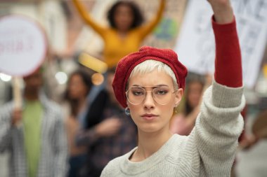 Kadın, kadın hakları için bir grup göstericiye yol gösteriyor. Genç güçlü kadın küresel bir grev sırasında protesto ediyor. Kameraya bakarak iklim değişikliğini protesto eden kızgın bir kızın portresi.. 
