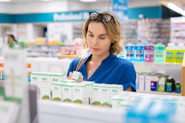 薬局で薬を選ぶ熟女 有効成分をチェックする女性 薬局で棚に薬の投与量 医療と健康の概念 — ストック写真
