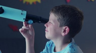 Ay yüzeyini araştırmak için teleskop kullanan meraklı çocuğun yüzünü kapatın. Küçük bir çocuk odasından galaksiyi görebilmek için geceleri teleskopla yıldızlara bakıyor. Küçük çocuk arka planda roketle dekore edilmiş odasında teleskopla yıldızları izliyor..