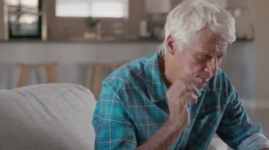 Acıdan muzdarip kıdemli adam kulaklarını tutuyor. Gergin, olgun bir adam evde oturmuş kulaklarını tutuyor. İşitme kaybı semptomu olan yaşlı adamın yan görüntüsü, kopyalama alanı. Olgun, emekli bir adam koltukta oturuyor parmakları kulağına yakın ve acı çekiyor..