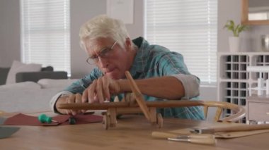 Ahşap uçak heykelini zımparalamak için zımpara kağıdı kullanıyor. Olgun marangoz evde ahşap uçuşlar yapıyor. Mutlu yaşlı büyükbaba evde el yapımı heykeller yapmakla meşgul..