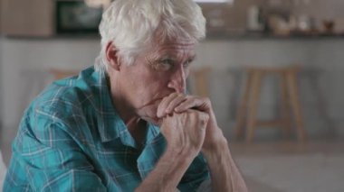 Evdeki kanepede yalnız ve düşünceli yaşlı bir adam oturuyor. Düşünceli emekli adam düşünüyor ve kameraya bakıyor. Mutsuz ve üzgün, beyaz saçlı, fotokopi odası olan yaşlı adam koltukta oturuyor..