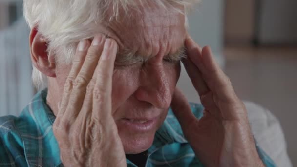 疲惫而又紧张的老人头脑清醒地坐在家里头疼 退休老人在家里担心健康问题 忧心忡忡的老人坐在家里头疼难忍 — 图库视频影像