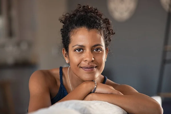 Confident indian woman relaxing on couch at home. Thoughtful smiling middle eastern girl sitting on sofa and looking at camera. Portrait of satisfied african american woman daydreaming at home with copy space.