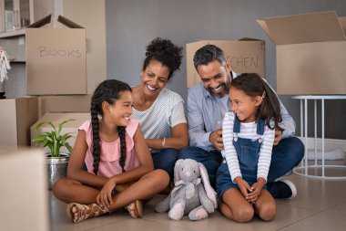 Cheerful young multiethnic parents talking and playing with daughters while sitting on floor in new house. Indian man family tickles and jokes with his little girl after relocating to new home. Happy family with two children having fun at new house a clipart