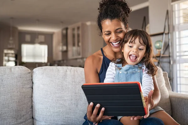 コピースペースのある自宅のデジタルタブレットで遊んでいる若い黒人の母親と笑顔の娘 若いですアフリカ系アメリカ人女性とともに陽気で興奮した女の子使用してデジタルタブレットしばらくリラックスオンソファ — ストック写真