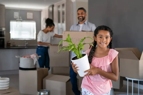 快乐的微笑着的女孩在新家种花 而印度的父亲在看着她 可爱的多民族女儿在新房子里看着相机时感到兴奋的画像 用植物装饰新房子的孩子 — 图库照片