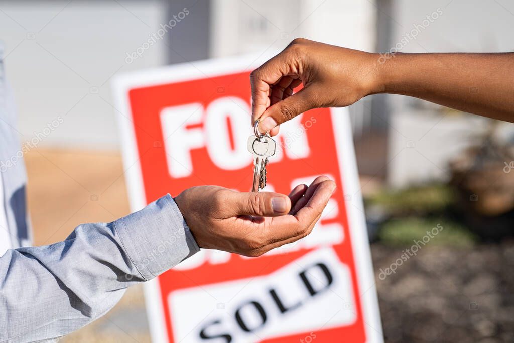 Saleswoman giving home keys to new property owner. Close up of real estate agent hand giving house keys to indian man. Agent giving apartment key to new owner after putting the word sold on for sale sign outside the house.