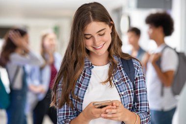 Lisenin kampüsünde akıllı telefon kullanan genç bir kadın. Gülümseyen üniversite öğrencisi koridorda cep telefonuyla mesajlaşıyor. Akıllı telefondan mesaj atan mutlu üniversiteli kız uygulaması kullanıyor..