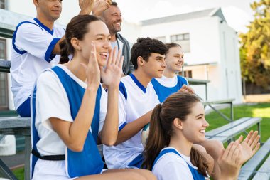Üniversite öğrencileri tribünde oturan futbol takımı için tezahürat yapıyor. Liseliler ve kızlar maç izlerken el çırpıyorlar. Bir grup taraftar stadyumun tribünlerinde bir spor müsabakasını izlerken takımı cesaretlendiriyor..