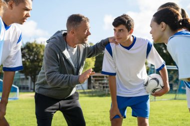 Futbol sahasındaki lise takımına olgunluk koçu öğretme stratejisi. Genç futbolcular bir arada duruyor ve koç motivasyon konuşmasını dinliyor. Koç, okul maçından önce takım tavsiyesi veriyor..
