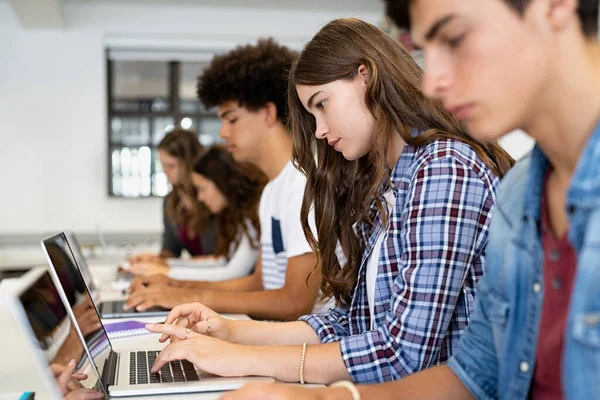 在课堂上 多族裔大学生坐在一个用笔记本电脑学习的教室里 一组男生和女生在计算机课上使用笔记本电脑 年轻的男人和聚精会神的女人成排地坐在一起做作业 — 图库照片