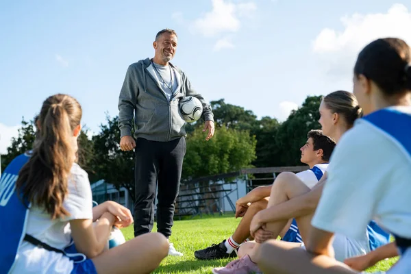 試合前にサッカーコーチがアドバイスをする サッカー場に座っているスポーツの先生の話を聞いている高校生 大学教授は若いサッカー選手にやる気のあるスピーチをする — ストック写真