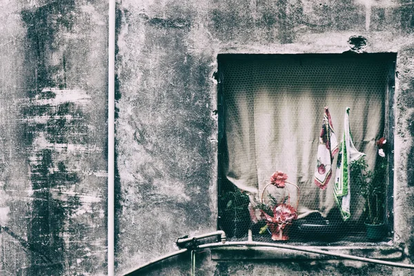 Janela de casa quadrada com flores e bandeiras em prédio pobre . — Fotografia de Stock