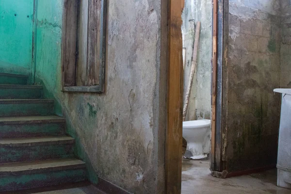 Worn bathroom near a decayed staircase in condemned building.