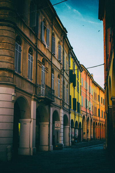 Low angle vertical photo of a stone street in an old Italian town with colorful houses and business edifices. No people.