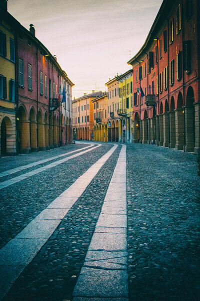 Low angle photo of a stone street in an old Italian town with colorful houses and business edifices with a pharmacy. No people.