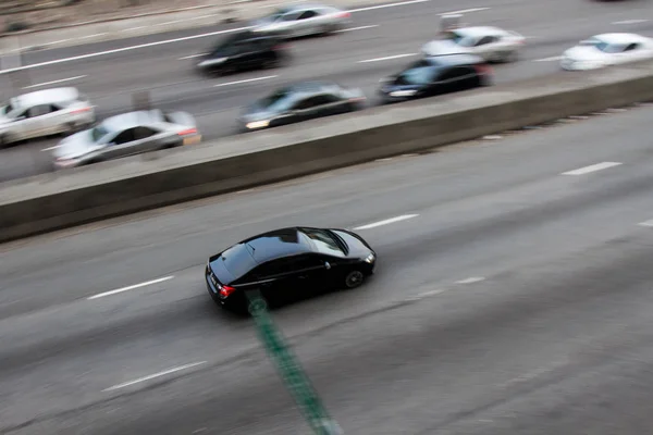 Pan çekim yön lane karşısında daha yavaş araba ile şehir merkezine yakın bir bina içinde bir cadde üzerinde bir siyah yüksek hızlı araba. Hiçbir insan.