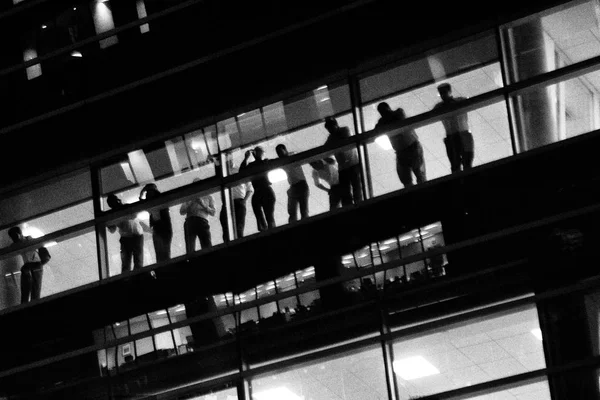 Urban black and white wallpaper background of people watching the street from a glass wall window of a modern architecture corporate building.