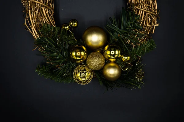 Wallpaper background texture of christmas wreath made of twig and golden balls and decorations with green branches isolated on black background.
