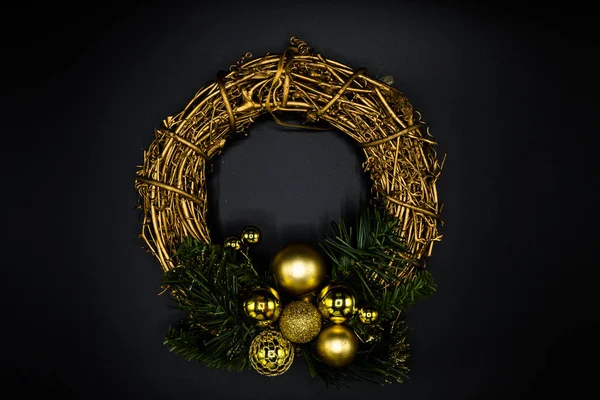 Wallpaper background texture of christmas wreath made of twig and golden balls and decorations with green branches isolated on black background.