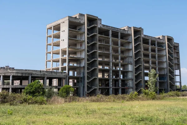 Huge multi floors concrete structure of abandoned building with stairs surrounded by grass and trees with blue sky in the background. Architecture detail. No people.