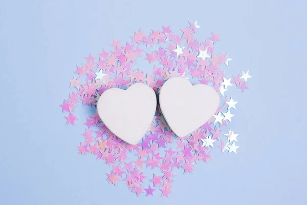Dağınık pembe glitter yıldız ile pastel mavi arka plan üzerinde iki beyaz kalp. Tasarımınız için aşk konsepti.