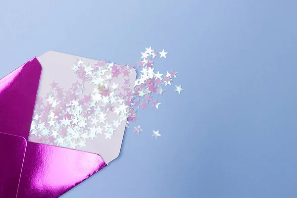 Mavi bir arka plan üzerinde bir form yıldız glitter konfeti ile parlak pembe zarf. Şenlikli konsept.