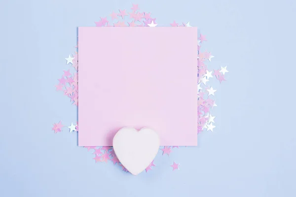 Beyaz ahşap kalp ve pastel pembe boş kart mockup dağınık pembe glitter yıldız ile pastel mavi arka plan üzerinde. Metniniz için yer.