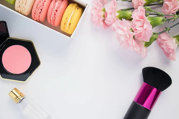Güzel renkli macaroons, parfüm, allık, fırça ve pembe karanfil çiçekler beyaz bir arka plan üzerinde. Izole.
