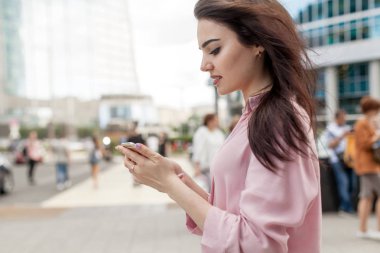 Mutlu oldukça esmer kız ya da istimal hareket eden telefon, telefon tarama ve online bir mobil uygulaması alışveriş merkezi yürüyüş gülümseyen süre alışveriş yaparken güzel kadın işkadını. Online iletişim