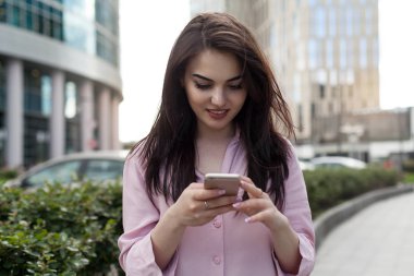 Gülümseyen güzel kadın sokak mutlu kız cep telefonu üzerinde Internet tarama ve satın alma sırasında bir giysi vitrin tarafından geçen smartphone kullanarak ve online alışveriş yaparken boyunca yürüyüş
