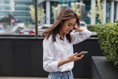 Mutlu oldukça esmer kız iş kadını istimal hareket eden telefon, telefon tarama ve online bir mobil uygulaması alışveriş merkezi yürüyüş gülümseyen süre alışveriş yaparken güzel kadın. Online iletişim.