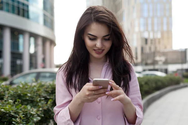 Gülümseyen güzel kadın sokak mutlu kız cep telefonu üzerinde Internet tarama ve satın alma sırasında bir giysi vitrin tarafından geçen smartphone kullanarak ve online alışveriş yaparken boyunca yürüyüş