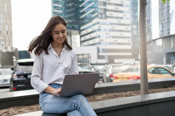 Onun laptop, gülümseyen ve ofis dışında oturan beyaz onun bilgisayar üzerinde ekonomik rapor yapıyor genç freelancer çalışan meşgul kadın. Kavramı Internet çalışmalarında ve başarı büyük bir şehirde