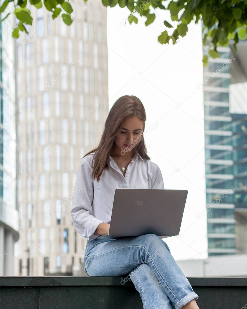 Beautiful hipster freelancer using laptop for work while sitting outside, brunette businesswoman using wireless connection working remotely on pc in the fresh air. Concept of remote and freelance work