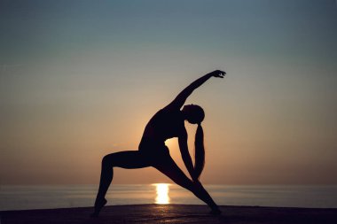 Gün batımında sahilde yalnız yoga uygulamak genç kadın silüeti. Mutluluk, fitness ve sağlıklı yaşam tarzı. Spor kız germe ve tatil sırasında açık havada egzersiz yapıyor