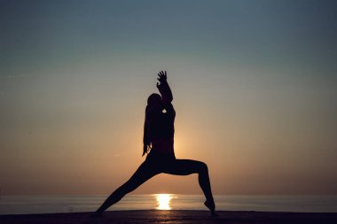 Gün batımında sahilde yalnız yoga uygulamak genç kadın silüeti. Kadın meditasyon, fitness ve sağlıklı yaşam tarzı. Spor kız germe ve tatil sırasında açık havada egzersiz yapıyor.