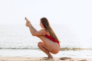 Esnek ve uygun olacak şekilde pratik yoga, bacak Germe genç kadın. Sağlıklı kız sahilde güneşin üzerinde yapıyor. Sabah erken rahatlatıcı. Calmless kavramı ve sağlık.