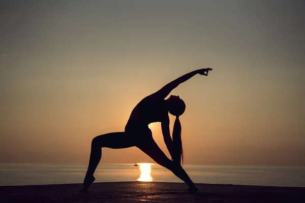 Akşam ise yoga yaparken ve germe pozlar pratik günbatımı üzerinde rahatlatıcı. Sağlıklı yaşam ve spor kavramı. Sahilde Deniz Manzaralı pier üzerine meditasyon.
