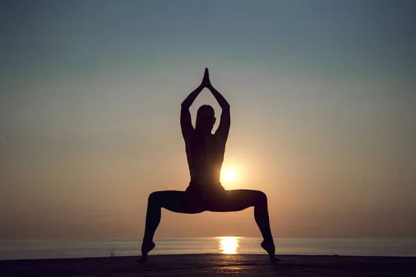 Yoga meditation woman silhouette on the ocean during amazing sunset. Woman doing stretching pilates outdoors to be healthy and live longer. Relaxing after a hard day and training. Healthy lifestyle.