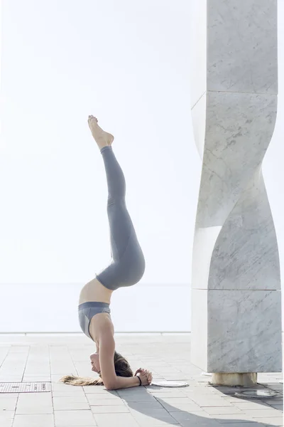 Kentsel dış headstanding pratik spor giyim güzel kız. Yoga yaparken ve arka plan üzerinde beyaz gökyüzü ile kafasına ayakta esnek kadın. Sakinlik, sakin ol, sağlıklı yaşam tarzı