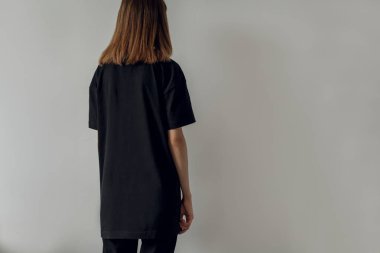 Genç hippi kız giyiyor siyah pantolon ve boş siyah t-shirt logo veya tasarım, model siyah t-shirt, arka plan, beyaz duvar için alan ile arkadan görünüm
